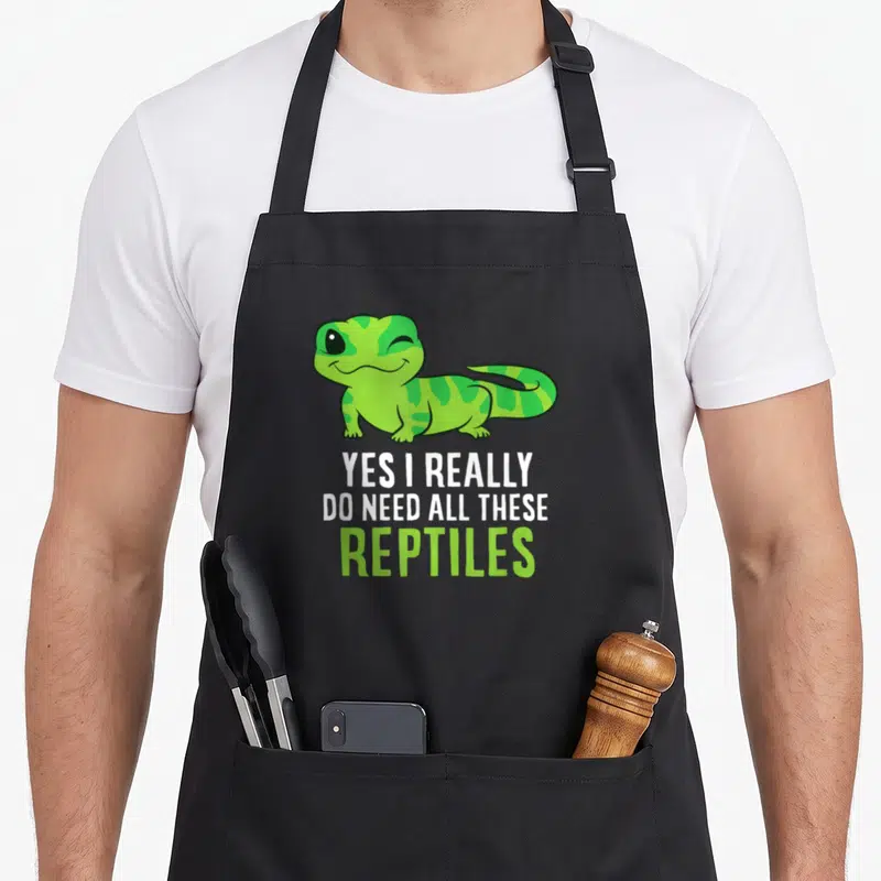 Reptile these apron - Cartoon gecko above stacked text YES I REALLY DO NEED ALL THESE REPTILES in lime and white — shown on a black cotton canvas apron against a white background