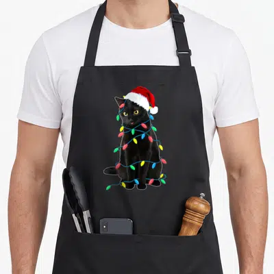 Kitten christmas tree apron - Black cat photo wearing red santa hat wrapped in blue string lights with red, green — shown on a black cotton canvas apron against a white background