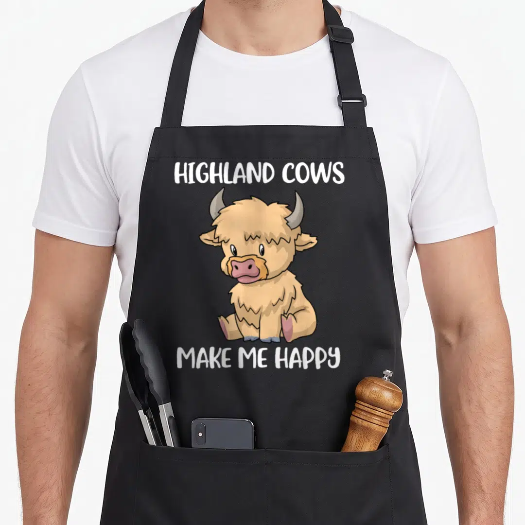 Messy highland cow apron - Cartoon tan sitting highland cow with white text reading HIGHLAND COWS MAKE ME HAPPY above — shown on a black cotton canvas apron against a white background