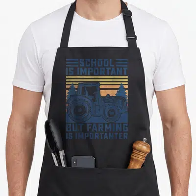 But farmer apron - Retro tractor illustration with blue lettering and striped orange-yellow-red sunset background — shown on a black cotton canvas apron against a white background