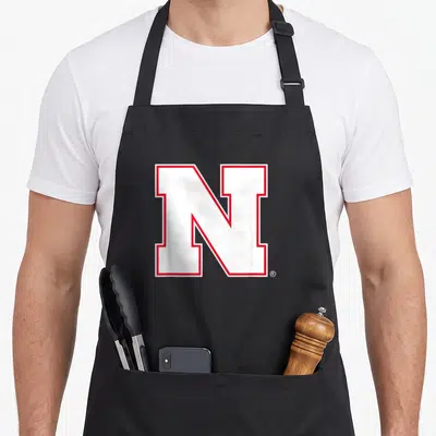 Icon nebraska girl apron - White capital letter N outlined in red — shown on a black cotton canvas apron against a white background