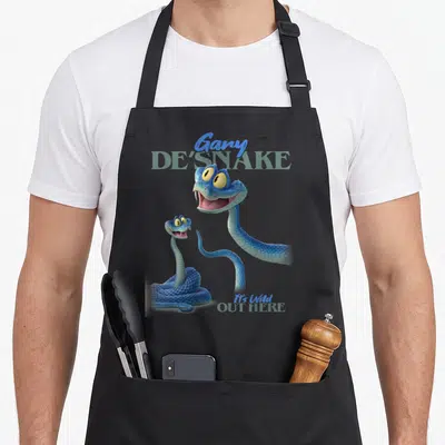 Desnake novelty apron - Two blue cartoon snakes with yellow eyes and text reading Gary De Snake It's Wild Out Here — shown on a black cotton canvas apron against a white background