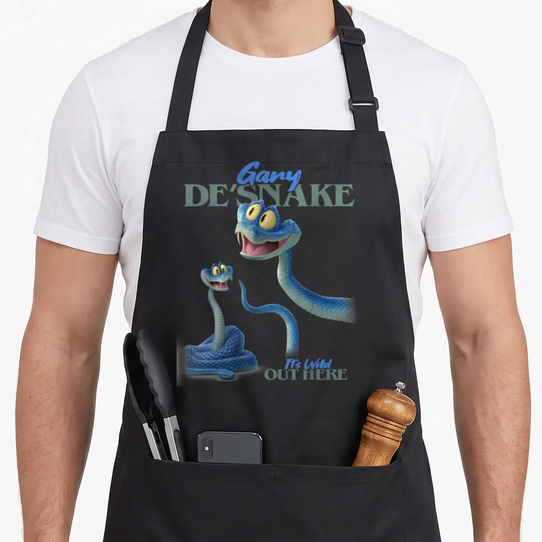 Desnake novelty apron - Two blue cartoon snakes with yellow eyes and text reading Gary De Snake It's Wild Out Here — shown on a black cotton canvas apron against a white background