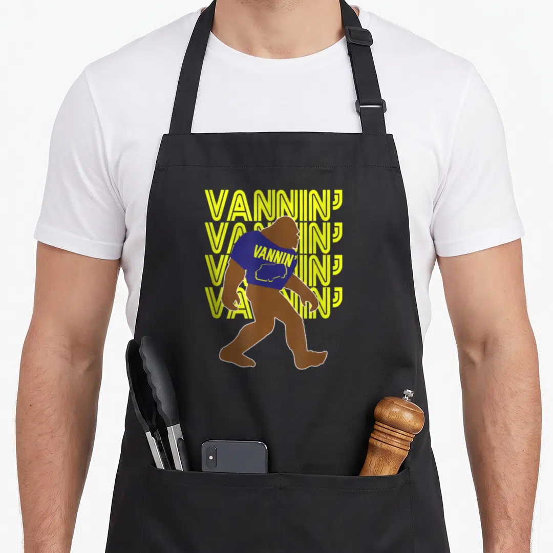 Vannin bigfoot apron - Brown Bigfoot in blue shirt with yellow VANNIN text stack — shown on a black cotton canvas apron against a white background