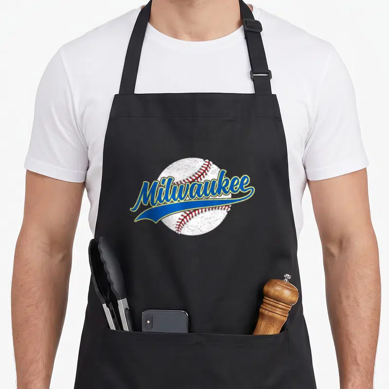 Funny baseball milwaukee apron - Retro Milwaukee script over white baseball with red stitching and blue swoosh — shown on a black cotton canvas apron against a white background