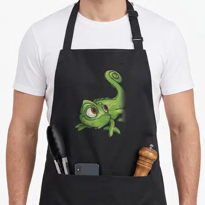 Pascal adorable aprons - Green cartoon chameleon with curled tail and large eyes centered on fabric — shown on a black cotton canvas apron against a white background