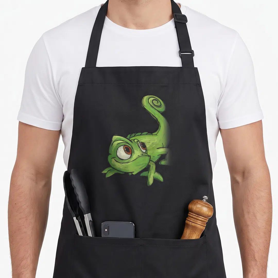 Pascal adorable aprons - Green cartoon chameleon with curled tail and large eyes centered on fabric — shown on a black cotton canvas apron against a white background