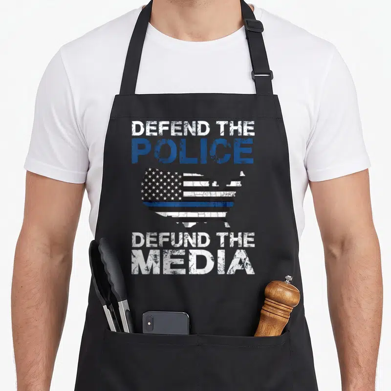 Defend police apron - Distressed USA map with thin blue line and text Defend The Police Defund The Media — shown on a black cotton canvas apron against a white background