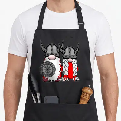 Nordic scandinavian aprons - Two cartoon gnomes in horned helmets, one holding a Vegvisir shield, red white grey design — shown on a black cotton canvas apron against a white background