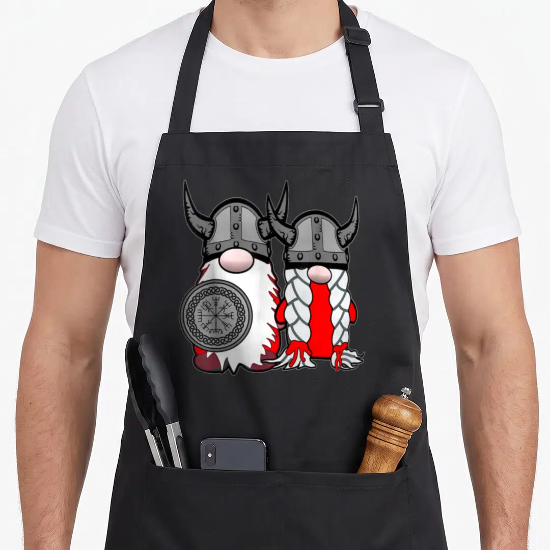 Nordic scandinavian aprons - Two cartoon gnomes in horned helmets, one holding a Vegvisir shield, red white grey design — shown on a black cotton canvas apron against a white background