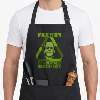 Recycled human made apron - Frankenstein head inside green recycle symbol with text made from 100% recycled human parts — shown on a black cotton canvas apron against a white background