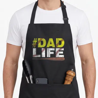 Softball baseball father day apron - #DAD LIFE text with baseball stitching and wooden bat on black background — shown on a black cotton canvas apron against a white background