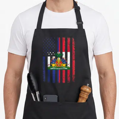 Haiti 4th of july apron - Distressed hybrid flag with US stars, Haitian stripes, central palm tree emblem, and L'UNION — shown on a black cotton canvas apron against a white background