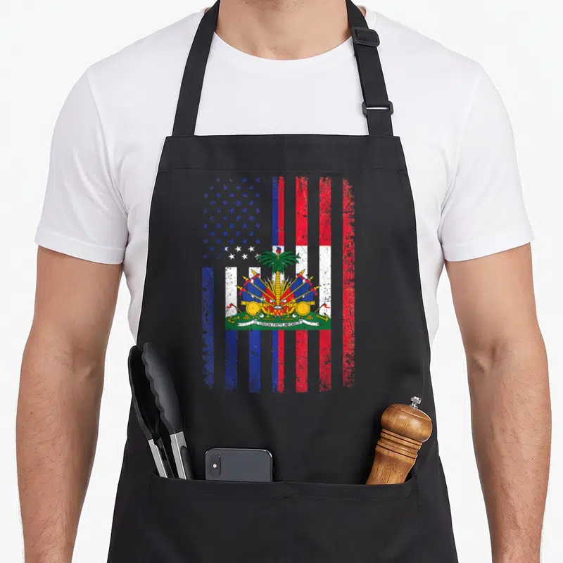 Haiti 4th of july apron - Distressed hybrid flag with US stars, Haitian stripes, central palm tree emblem, and L'UNION — shown on a black cotton canvas apron against a white background