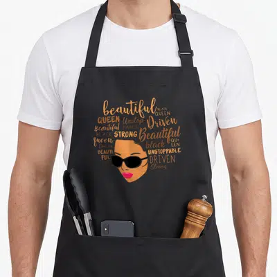 Beautiful magic apron - Woman face with sunglasses surrounded by beautiful black queen unstoppable driven strong orange — shown on a black cotton canvas apron against a white background
