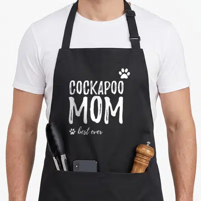 Retro dog cockapoo apron - White COCKAPOO MOM best ever text with three paw prints in typography only style — shown on a black cotton canvas apron against a white background