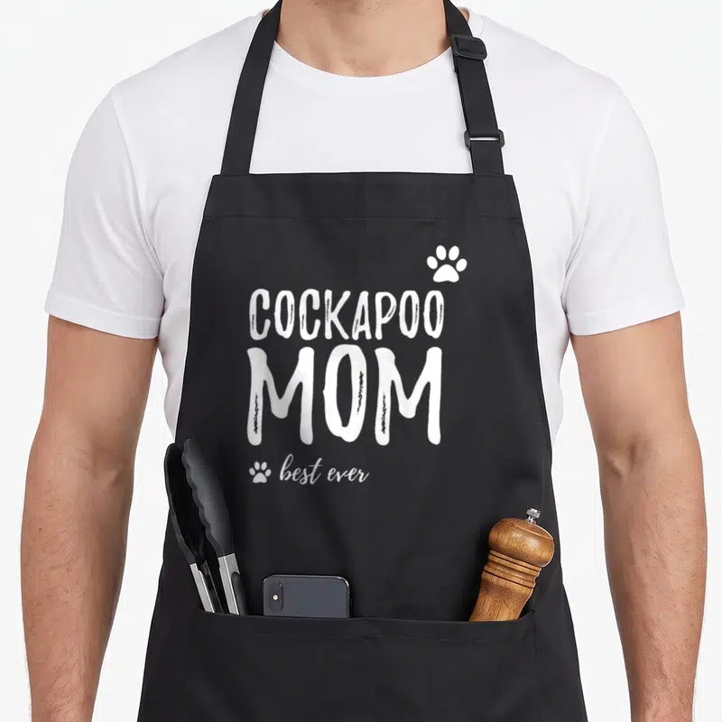Retro dog cockapoo apron - White COCKAPOO MOM best ever text with three paw prints in typography only style — shown on a black cotton canvas apron against a white background