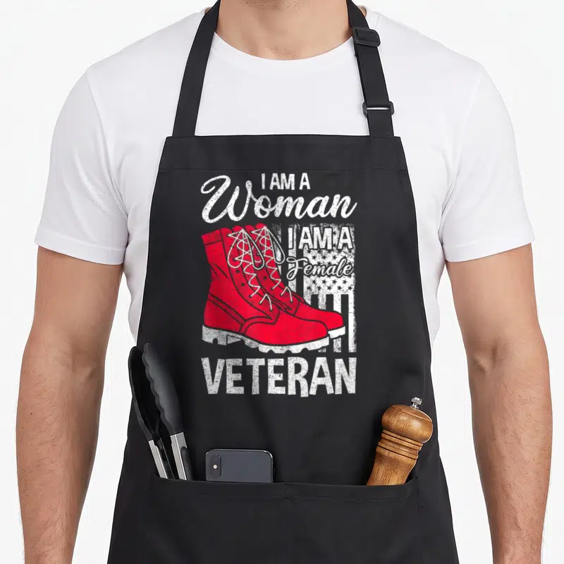 Soldier veteran patriotic apron - Red combat boots with I AM A Woman Female Veteran text and distressed flag pattern — shown on a black cotton canvas apron against a white background