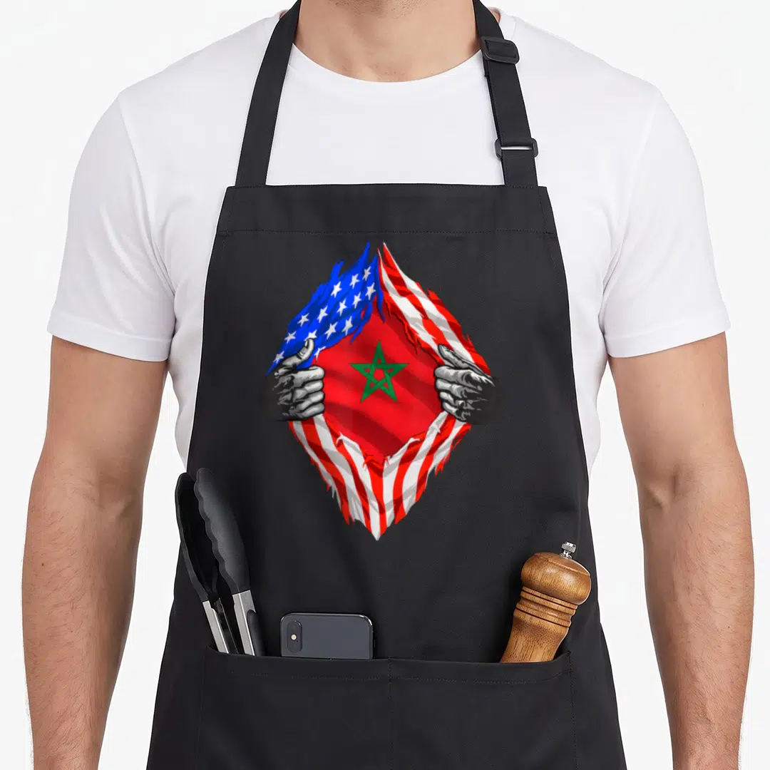 Moroccan root american flag apron - Two hands tearing a USA flag to reveal a Moroccan flag with a green star in red — shown on a black cotton canvas apron against a white background
