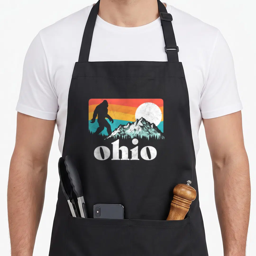 State bigfoot pride apron - Distressed white ohio text below grey creature silhouette and mountain graphic — shown on a black cotton canvas apron against a white background