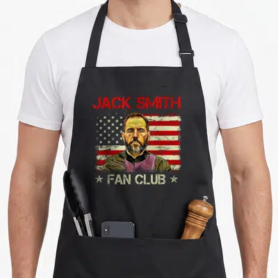 Jack american flag apron - Distressed USA flag behind man portrait with Jack Smith Fan Club text and white stars — shown on a black cotton canvas apron against a white background