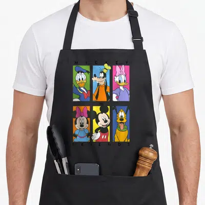 Shot friends cooking apron - Six cartoon characters in red, blue, yellow, pink, and green vertical bars with centered — shown on a black cotton canvas apron against a white background