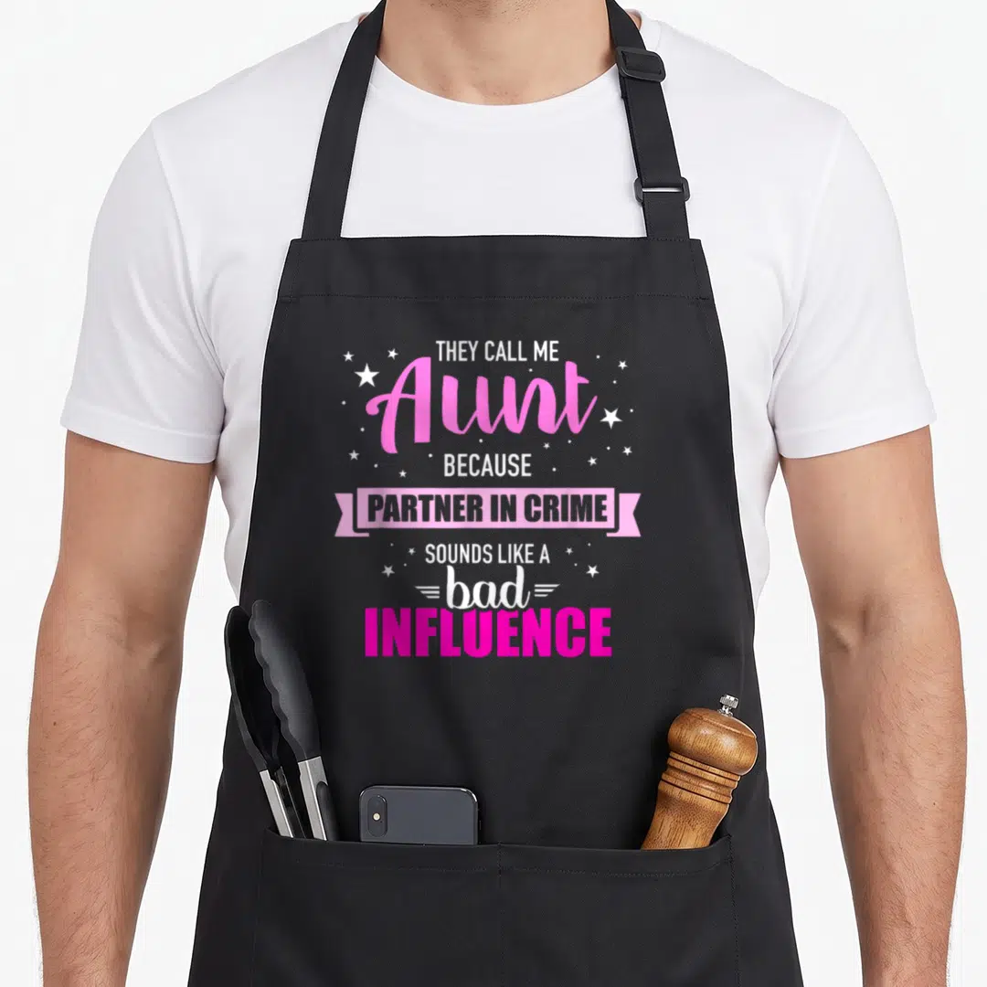 Aunt sound apron - Stacked pink and white text reading partner in crime inside a ribbon banner with scattered stars — shown on a black cotton canvas apron against a white background