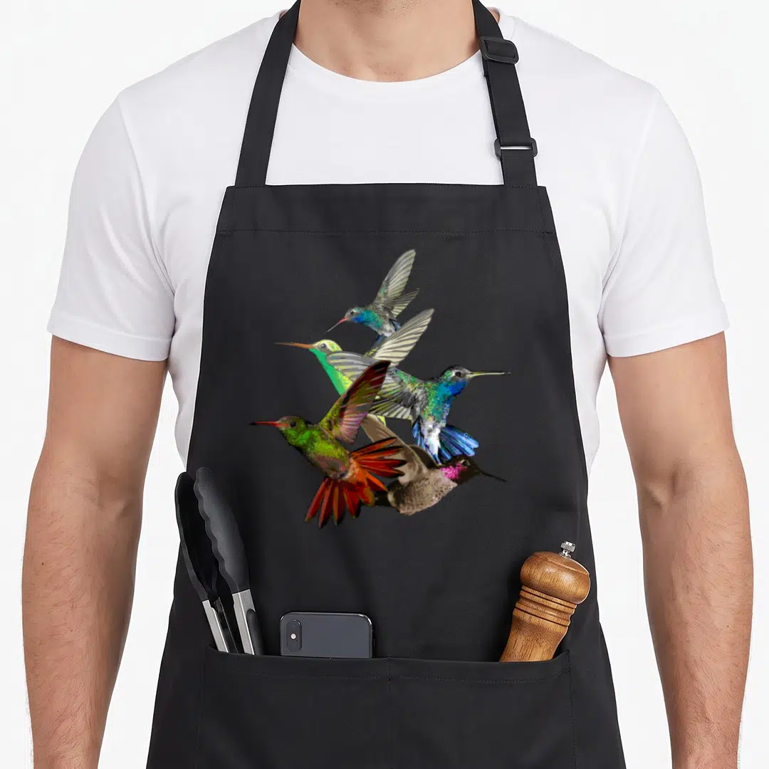 Hummingbird bird apron - Five realistic hummingbirds in blue, green, red, and brown clustered in flight — shown on a black cotton canvas apron against a white background