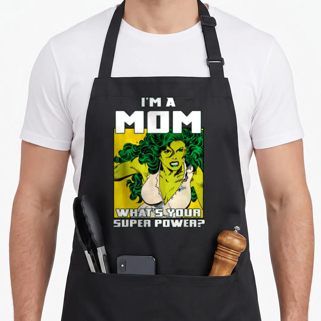 She mother's day aprons - Cartoon green woman yellow background I'M A MOM WHAT'S YOUR SUPER POWER text — shown on a black cotton canvas apron against a white background