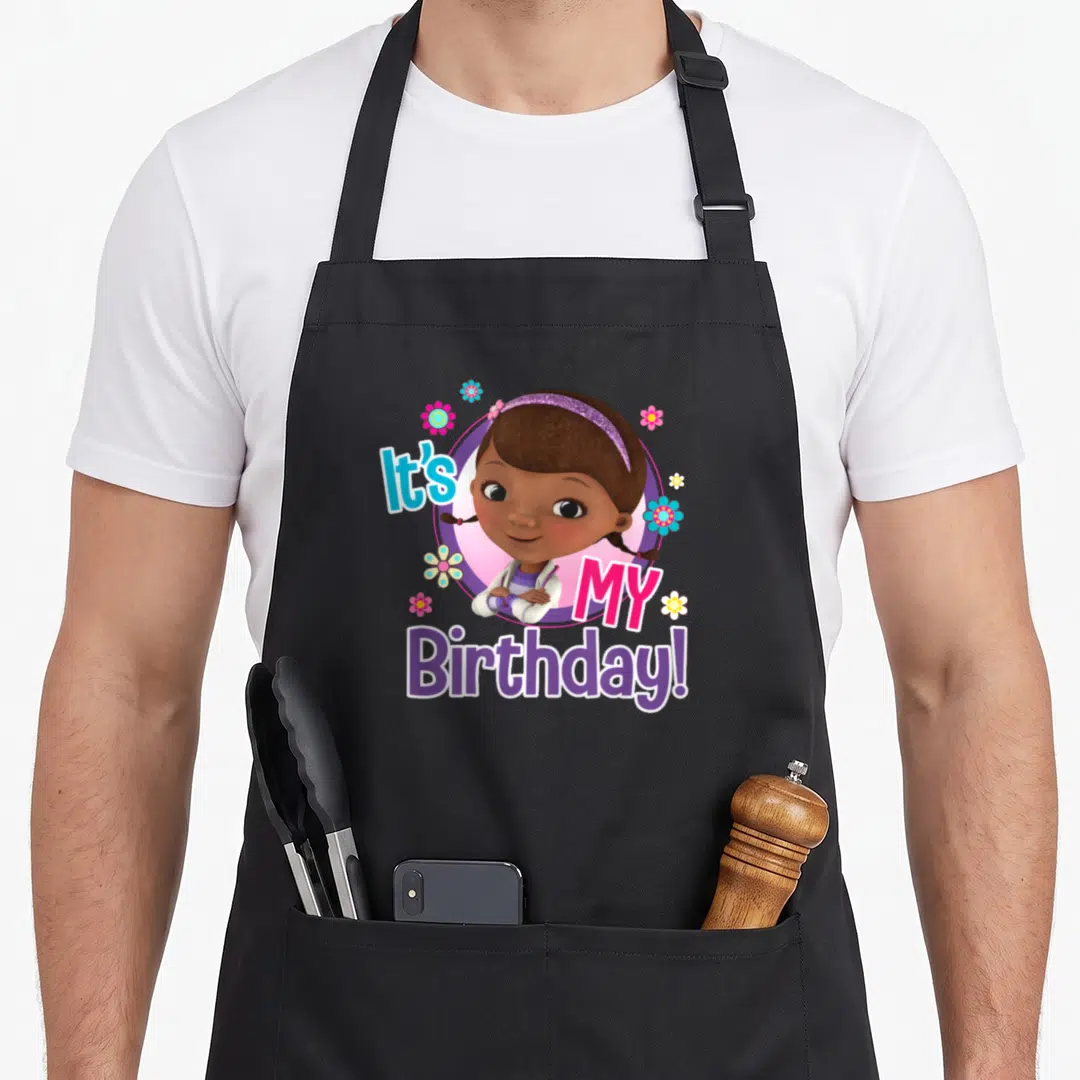 Doc junior apron - Cartoon girl in purple circle with It's MY Birthday text and pink blue flowers — shown on a black cotton canvas apron against a white background