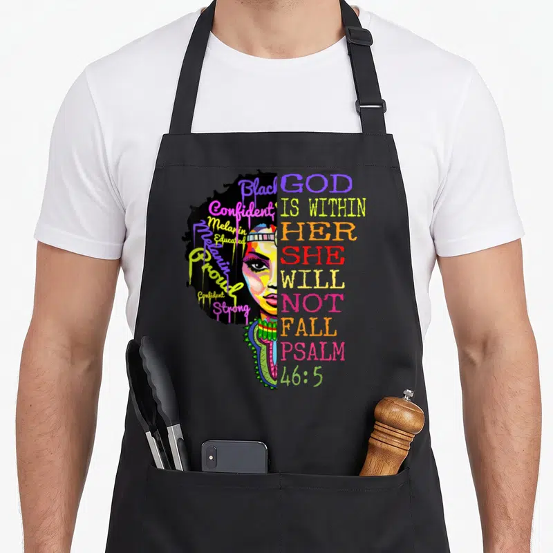 God fall apron - Cartoon woman face with colorful affirming words in hair next to stacked Psalms 46:5 text — shown on a black cotton canvas apron against a white background