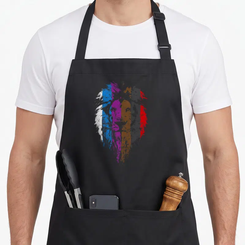 Belt lion apron - Distressed lion head formed by vertical stripes in white, blue, purple, brown, grey, and red — shown on a black cotton canvas apron against a white background