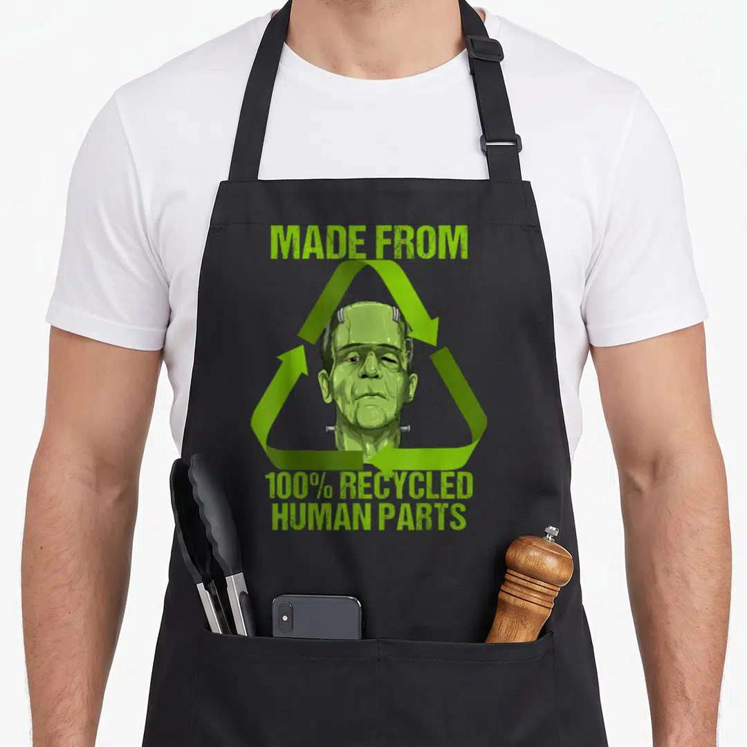 Frankenstein human made apron - Lime green recycling symbol enclosing a Frankenstein monster head with stacked text — shown on a black cotton canvas apron against a white background