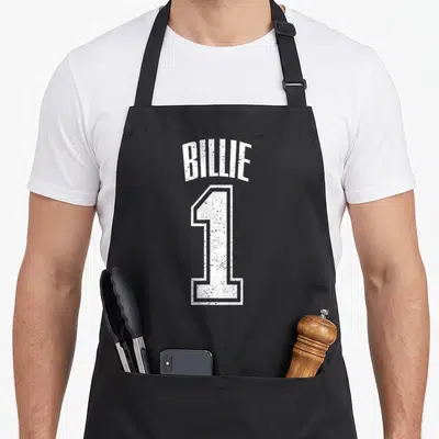 Billie sports fan apron - Arched BILLIE text above a large distressed white number 1 outline — shown on a black cotton canvas apron against a white background