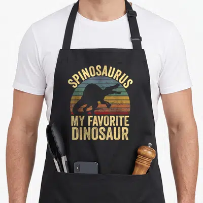 Spinosaurus dino dinosaur apron - Retro striped sun with Spinosaurus silhouette and My Favorite Dinosaur text — shown on a black cotton canvas apron against a white background