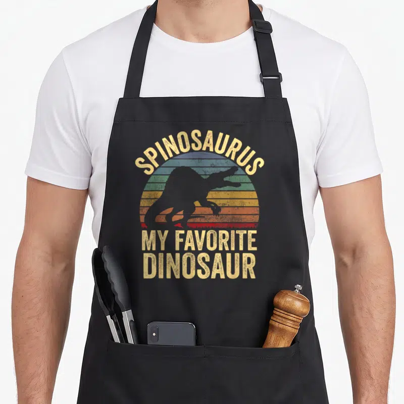 Spinosaurus dino dinosaur apron - Retro striped sun with Spinosaurus silhouette and My Favorite Dinosaur text — shown on a black cotton canvas apron against a white background