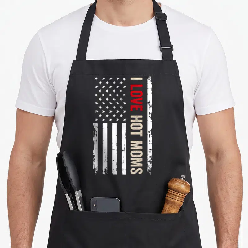 Hot american flag apron - Vertical I Love Hot Moms text over distressed USA flag in red and beige — shown on a black cotton canvas apron against a white background