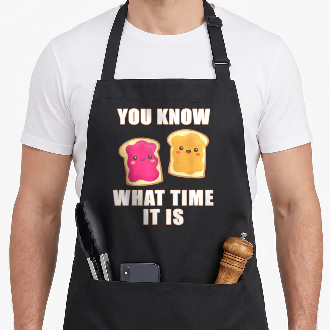 Much butter apron - Two cartoon toast slices with pink jam and yellow spread under white text reading YOU KNOW WHAT — shown on a black cotton canvas apron against a white background