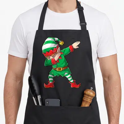 Xmas christmas elf apron - Cartoon elf dabbing in green red white and yellow stripes — shown on a black cotton canvas apron against a white background