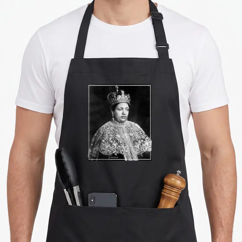 Empress ethiopian apron - Grayscale portrait of a queen in a crown and ornate cape with Queen text at the bottom — shown on a black cotton canvas apron against a white background