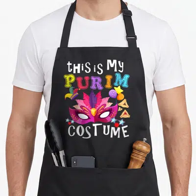 Purim jewish apron - Colorful mask surrounded by jester hat, balloons, hamantaschen, stars with text this is My PURIM — shown on a black cotton canvas apron against a white background