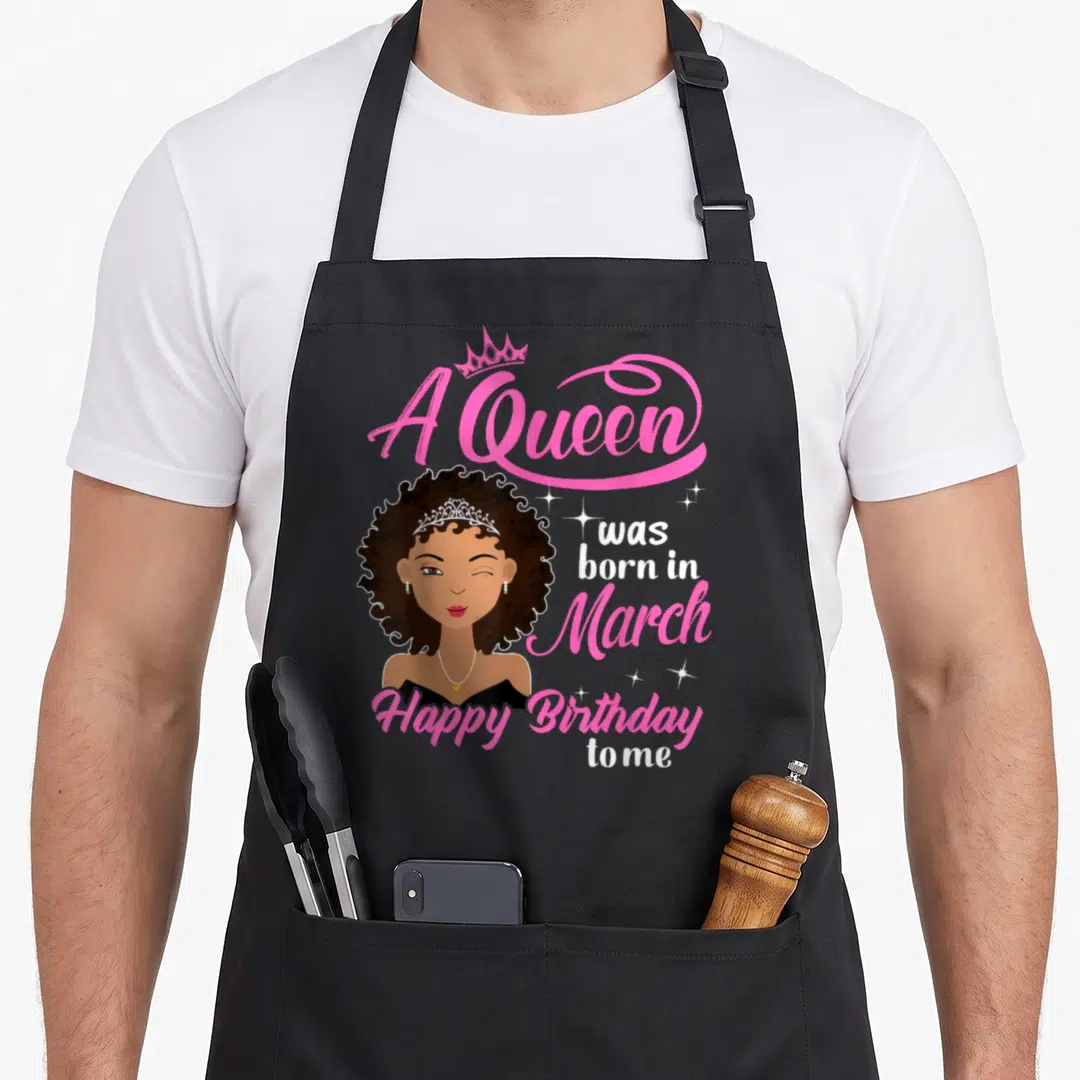 Cute march baking queen apron - Cartoon woman winking with A Queen was born in March text in pink and white — shown on a black cotton canvas apron against a white background