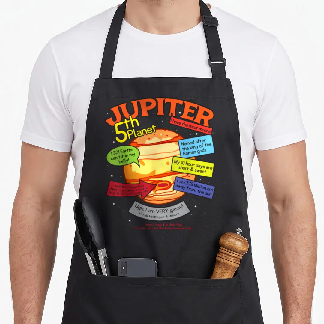 Learning teaching apron - Cartoon Jupiter planet with colorful speech bubbles listing facts about moons, rings — shown on a black cotton canvas apron against a white background