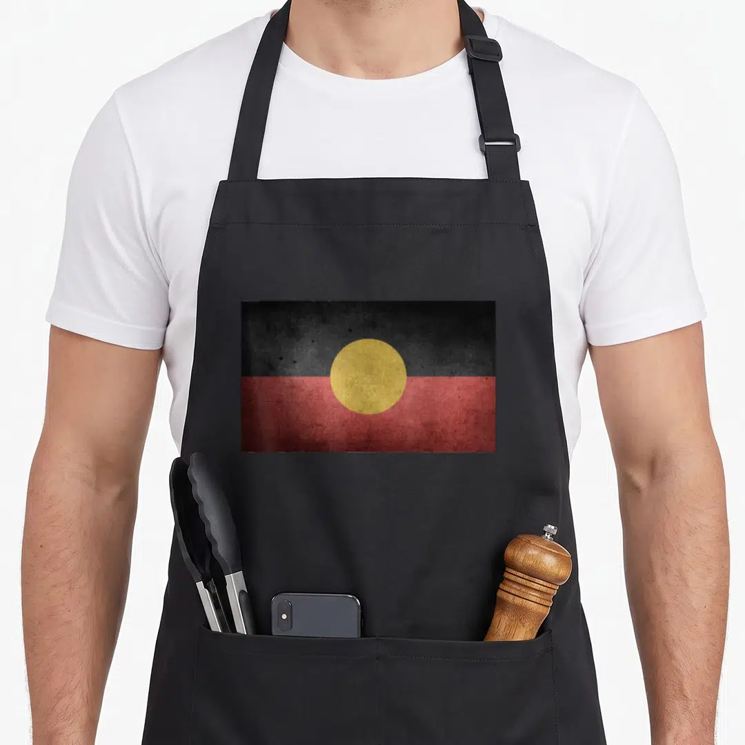 Dreamtime australian apron - Distressed Aboriginal flag with black top, red bottom, and yellow circle center — shown on a black cotton canvas apron against a white background