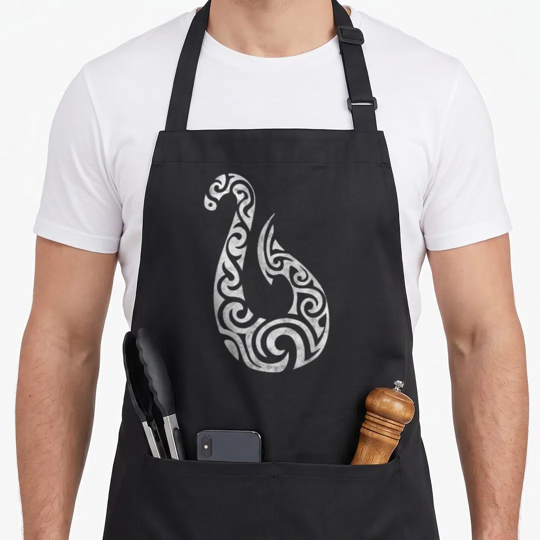 Polynesian new zealand apron - White line-art tribal fish hook swirl centered on grey background — shown on a black cotton canvas apron against a white background