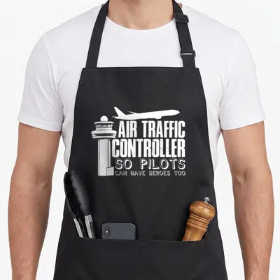 Ladder aviation apron - White control tower and flying plane silhouette with stacked text reading air traffic — shown on a black cotton canvas apron against a white background