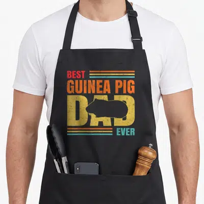 Father pet apron - Retro BEST GUINEA PIG DAD EVER text with guinea pig silhouette in red orange yellow blue — shown on a black cotton canvas apron against a white background