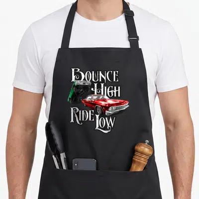 Bounce car apron - Red and green lowrider cars with BOUNCE HIGH RIDE LOW text in white gothic font — shown on a black cotton canvas apron against a white background