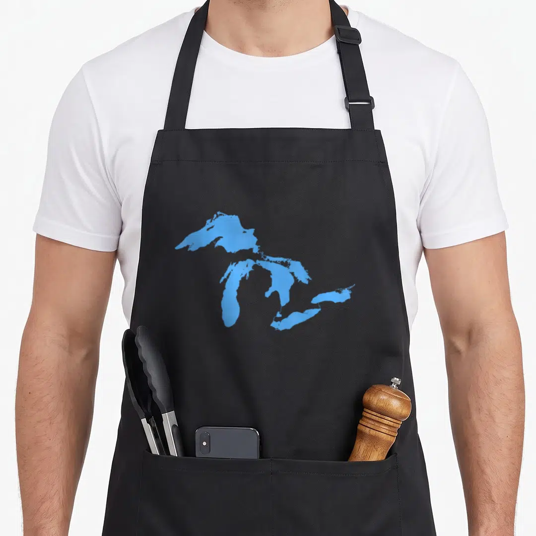 Funny lake michigan apron - Minimalist blue silhouette of the Great Lakes centered on grey background — shown on a black cotton canvas apron against a white background