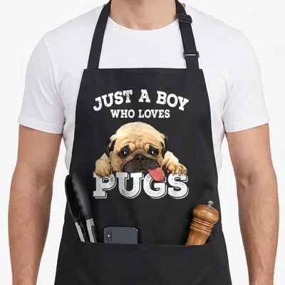 Vintage pug dog apron - Realistic tan and black pug resting paws on white Just a Boy Who Loves Pugs text — shown on a black cotton canvas apron against a white background